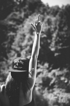 black and white photograph of a woman with her hand up in the air while wearing a hat