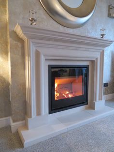 a fireplace with a fire burning in it next to a wall mounted mirror and clock