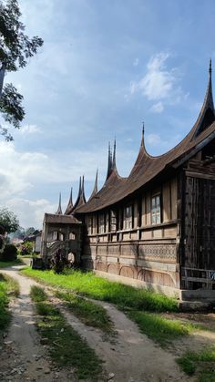 an old wooden building sitting on top of a lush green field next to a dirt road