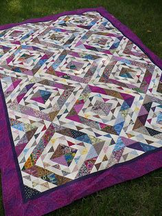 a quilt is laying on the ground in the grass with it's purple border