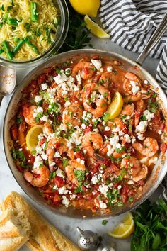 a skillet filled with shrimp, feta cheese and garnished with lemon wedges