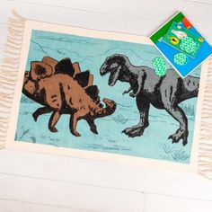 the rug has dinosaurs on it and is next to a book with an image of a dinosaur