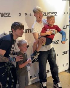 two boys and one boy are posing for a photo with each other in front of a wall