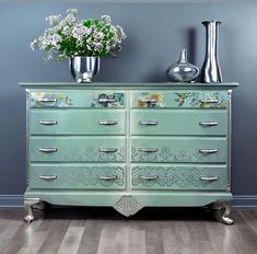 a green dresser with flowers and vases on top