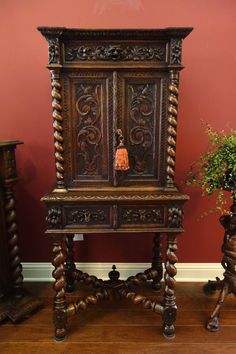 an ornate wooden cabinet next to a potted plant on the floor in front of a red wall