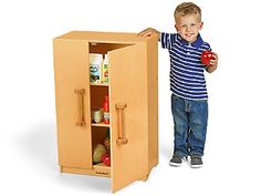 a young boy holding an apple and standing next to a cabinet with its doors open