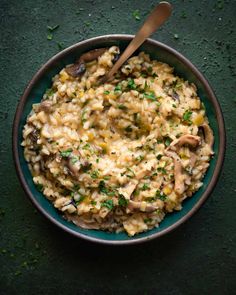 a bowl filled with rice and mushrooms on top of a green table next to a wooden spoon