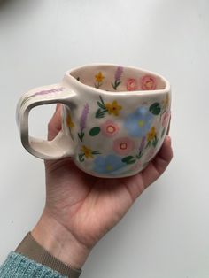 a hand holding a cup with flowers painted on it