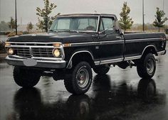 an old black pickup truck parked in a parking lot on a rainy day with no one around