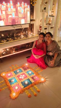 two women are sitting on the floor in front of a decorated cake with lit candles