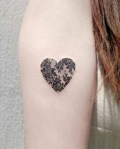 a black and white heart tattoo on the left upper arm, with an intricate lace design