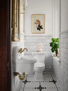 a white toilet sitting next to a sink in a bathroom under a framed painting on the wall