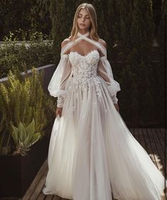 a woman in a white dress standing on a wooden deck wearing an off - the - shoulder gown