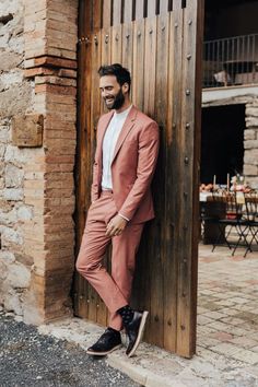 a man in a pink suit leaning against a wooden door with his foot on the ground