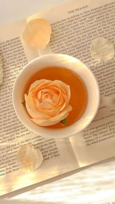 a cup of tea with a rose in it sitting on top of an open book