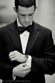 a young man in a tuxedo adjusts his cuff on his suit jacket