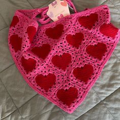 a pink crocheted bag with red hearts on it sitting on top of a bed