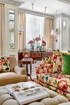 a living room filled with lots of furniture and flowers on the couches in front of two windows