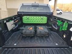 the back end of a black truck with two green tool boxes in it's trunk