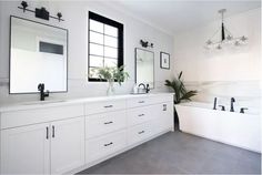 a white bathroom with two sinks and a bathtub in the middle, surrounded by black framed windows