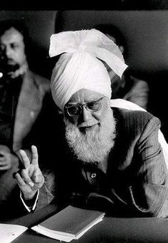 an old man with a turban sitting at a table in front of other men