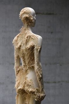 a mannequin is made out of wood and feathers on display in front of a concrete wall