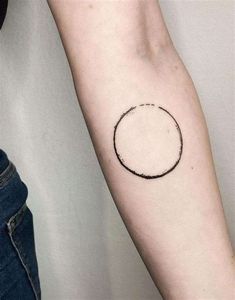 a small black circle tattoo on the arm