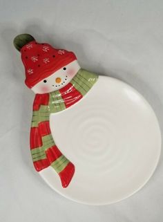 a white plate with a red and green snowman decoration on the edge, sitting on a white surface