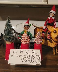 two elf figurines sitting on top of red plastic cups next to a sign that says it's real or is it cake?