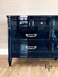 a dark blue dresser with brass handles and knobs on the drawers is sitting on a wooden floor