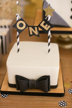 a white cake with black and gold decorations on it's top that says one