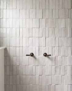 a white tiled bathroom with two handles on the wall