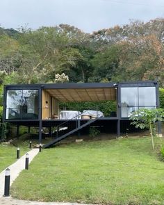 a house made out of shipping containers sitting on top of a lush green field next to trees