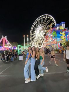 three women hugging each other in front of an amusement park ferris wheel and carnival rides