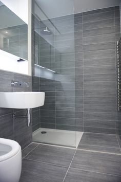 a bathroom with grey tiles and white fixtures, including a sink and shower stall in the corner