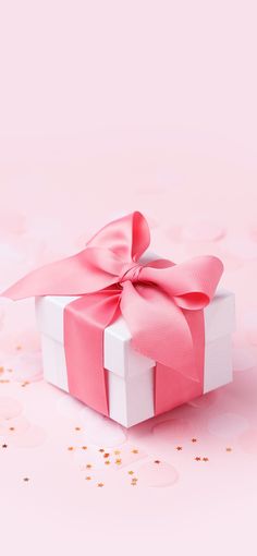 a pink and white gift box with a bow on it's side, surrounded by confetti sprinkles