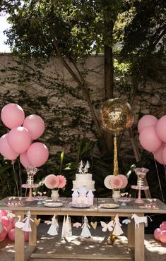 a table topped with lots of pink balloons next to a cake and cupcakes