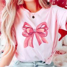 Embrace elegance and flirtatious charm with our captivating pink bow shirt, a delightful addition to your coquette-inspired wardrobe! 🌸👚 This shirt embodies the essence of femininity and playfulness, perfect for those who adore a touch of chic sophistication with a hint of flirtation. 🌷 The darling pink hue complements the shirt's design, accentuating the focal point--an exquisitely crafted oversized bow adorning the neckline or sleeves, adding a whimsical and flirtatious allure to your ensem Feminine Pink Crew Neck T-shirt, Cute Bow T-shirt For Spring, Feminine Pink Summer Shirt, Feminine Pink Shirt For Summer, Spring Party Tops With Ribbon, Feminine Party Tops With Bow Detail, Cute Pink T-shirt With Bow, Feminine Tops With Ribbon For Spring, Feminine Ribbon Tops For Spring