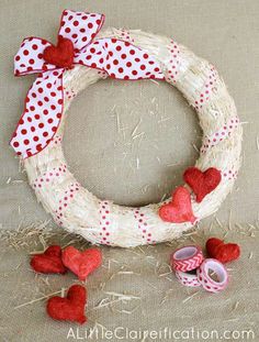 a white wreath with red hearts on it next to some twine and two rolls of tape