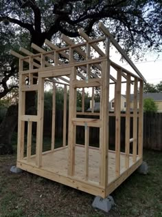 a small wooden structure sitting in the middle of a yard next to a large tree