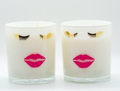 two white candles with pink lipstick and gold eyelashes on them, one has eyes closed