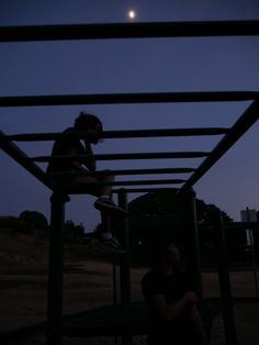 a woman sitting on top of a metal structure next to a person in the dark