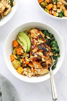 two bowls filled with chicken and vegetables on top of a white table next to silverware