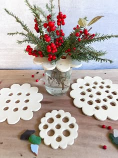 a vase filled with red berries and greenery next to cut out snowflakes