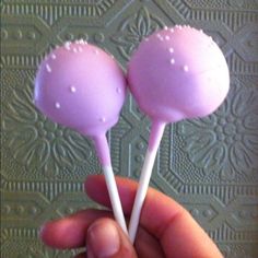 two pink lollipops with white sprinkles on them are being held by a hand