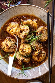 a bowl filled with dumplings covered in sauce and garnished with green onions