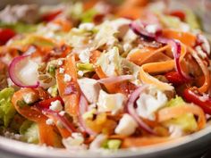 a salad with carrots, lettuce, onions and feta cheese in a bowl