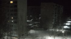 a city street is covered in snow at night with buildings and cars on the other side