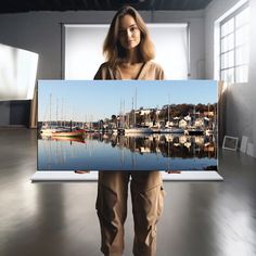 a woman is holding up a photo of boats in the water with her hands behind her back