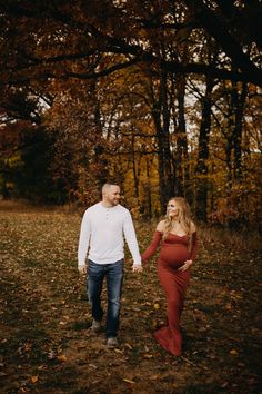 a pregnant couple holding hands and walking through the woods during their fall engagement session in ottawa, canada